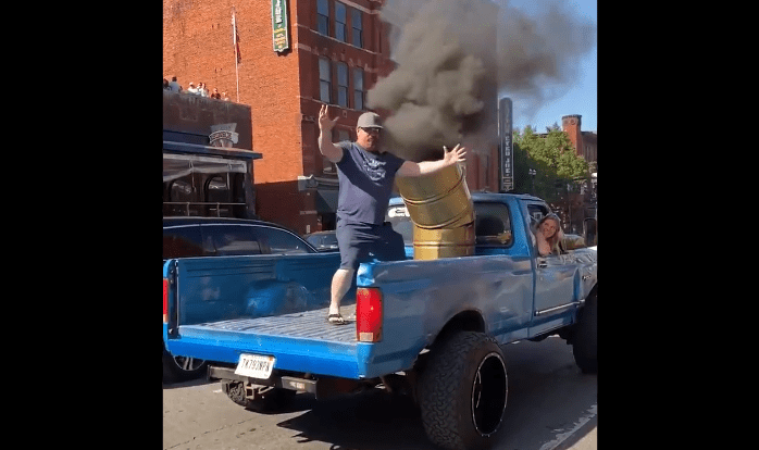 A person standing on a car with a barrel on top of it
