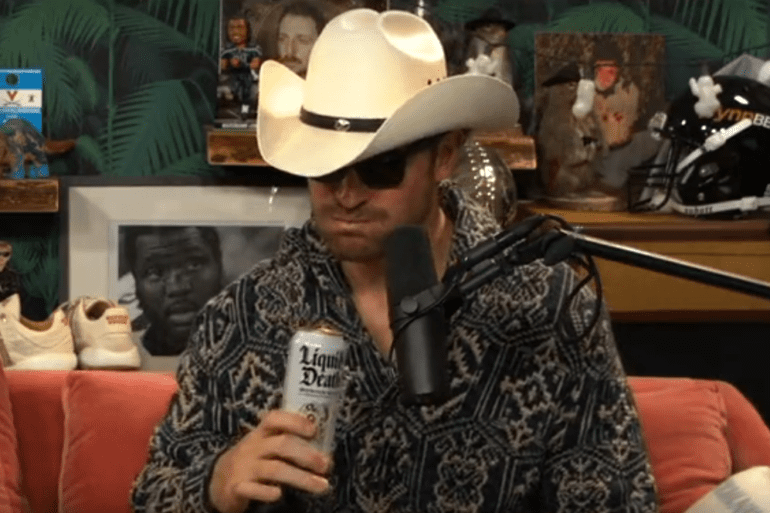 A person wearing a cowboy hat and sunglasses holding a bottle of beer