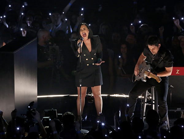 A woman singing on a stage with a man playing guitar and a microphone