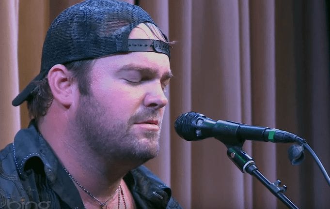 Lee Brice with a beard and a hat with a microphone in front of him