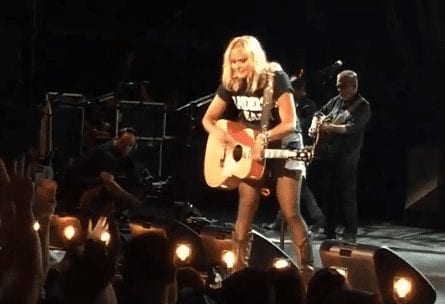 A person playing a guitar on a stage with a crowd watching