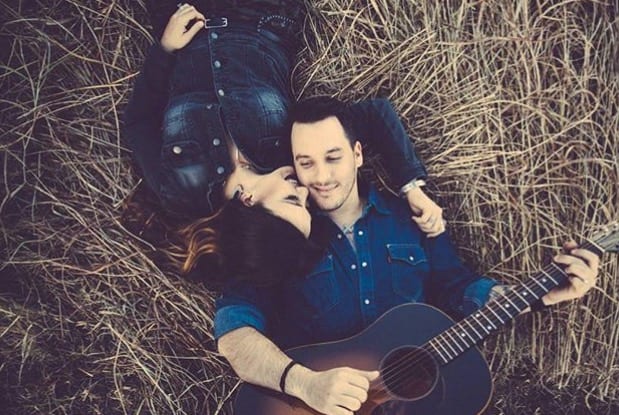 A man and a woman sitting on a bench with a guitar