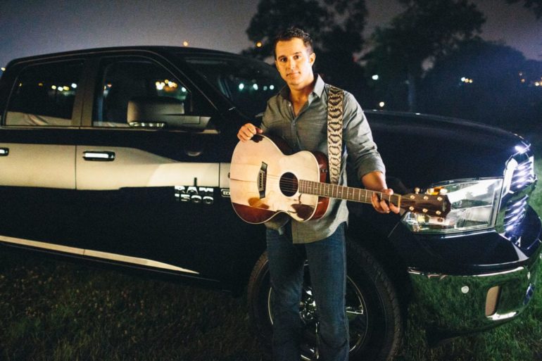 Easton Corbin playing a guitar next to a car