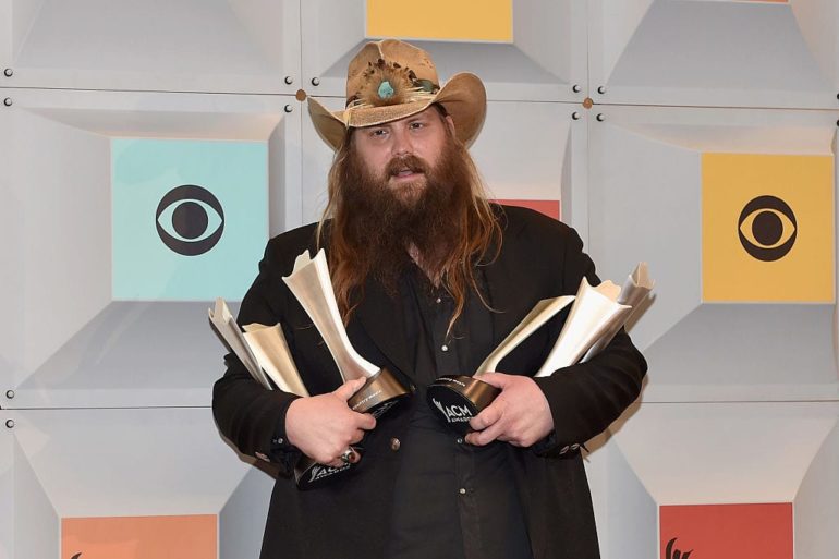 Chris Stapleton with a hat and a beard holding a gun
