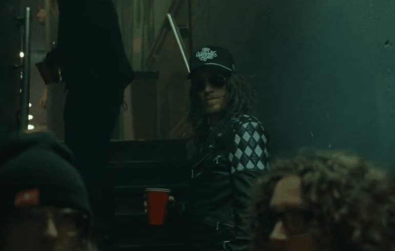 A person with long hair and a hat in a dark room with people