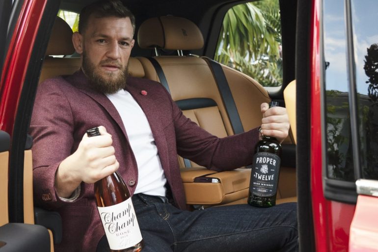 Conor McGregor sitting in a car holding a bottle of alcohol