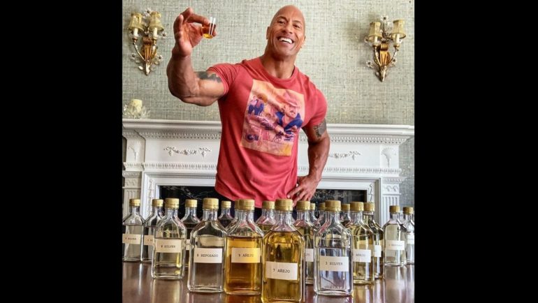 Dwayne Johnson standing next to a display of liquor bottles