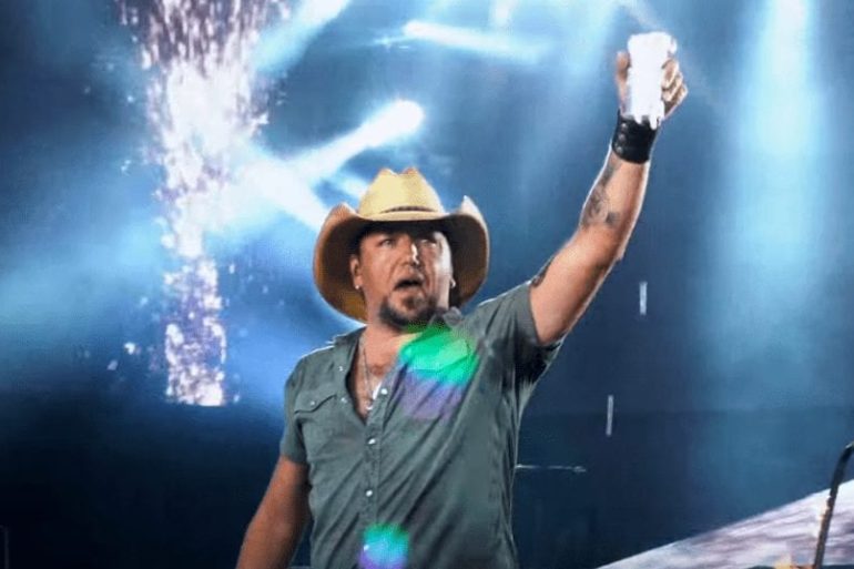 Jason Aldean with a hat and a microphone in front of a stage with lights