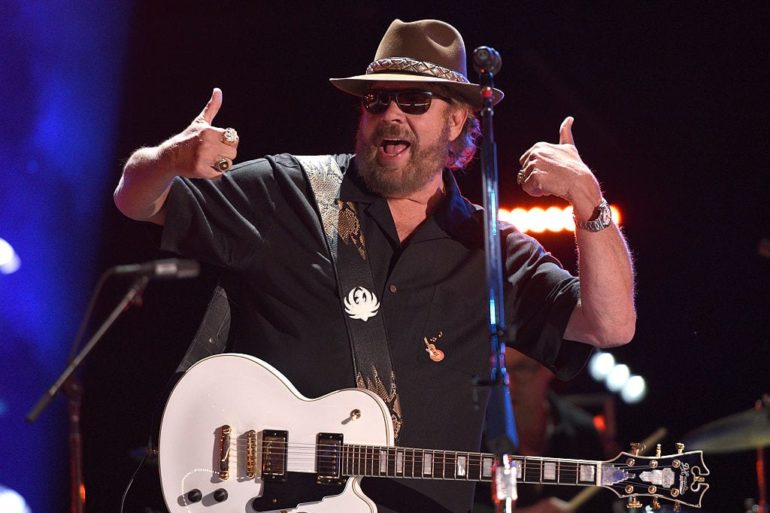 Hank Williams Jr. with a hat and sunglasses playing a guitar