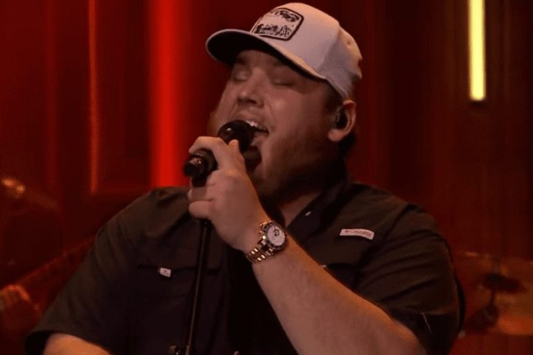 Luke Combs wearing a hat and holding a microphone