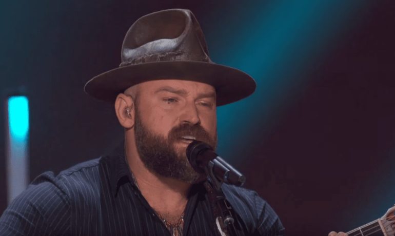 Zac Brown with a beard and a hat singing into a microphone