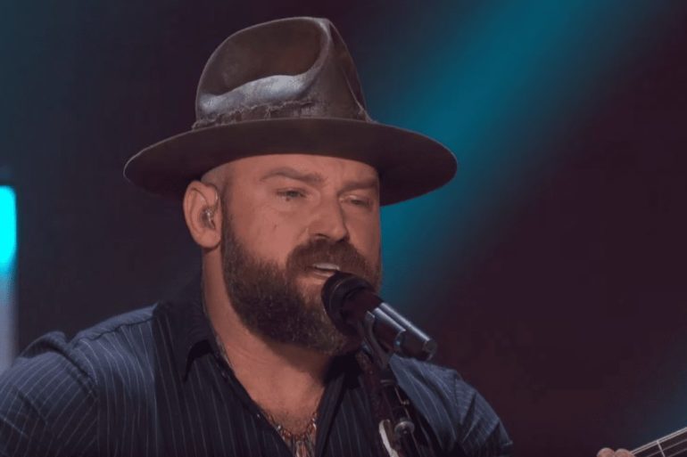 Zac Brown with a beard and a hat singing into a microphone