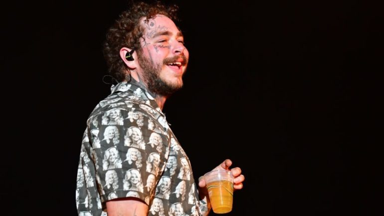 Post Malone with curly hair holding a drink