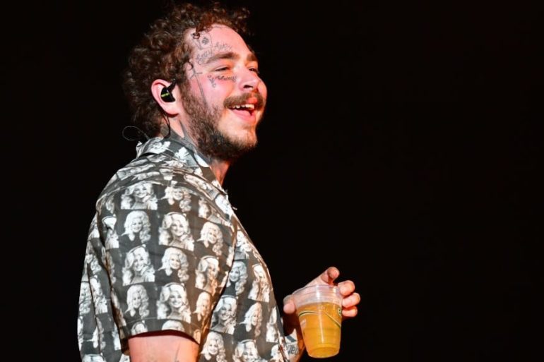 Post Malone with curly hair holding a drink
