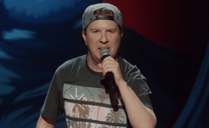 Nick Swardson wearing a hat and holding a microphone