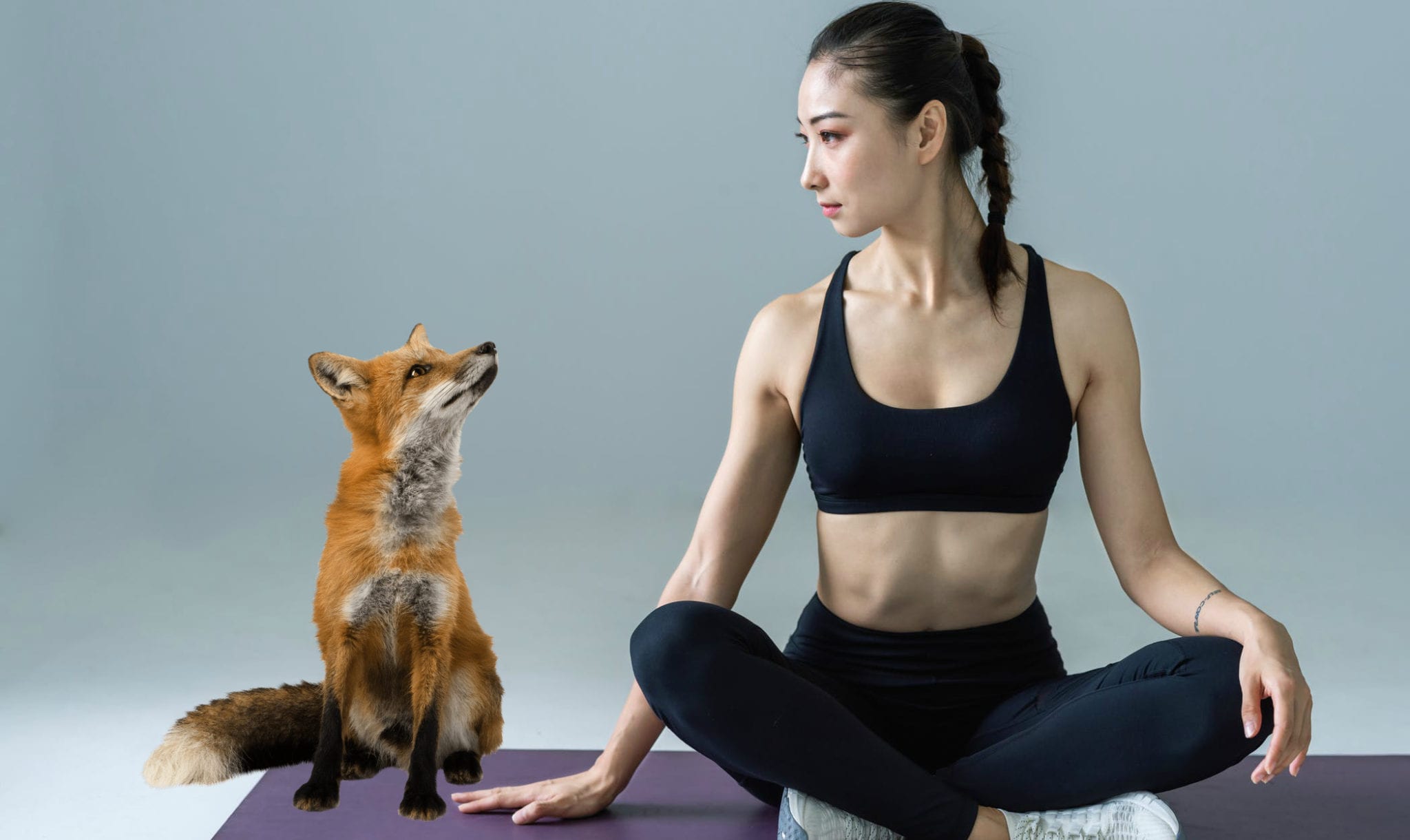 A woman sitting on a yoga mat next to a dog