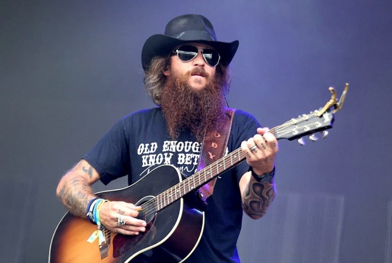 A man with a beard and a hat playing a guitar