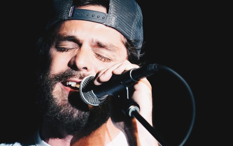 Thomas Rhett with a beard and a hat singing into a microphone