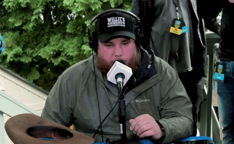 Luke Combs wearing a hat and headphones playing a guitar