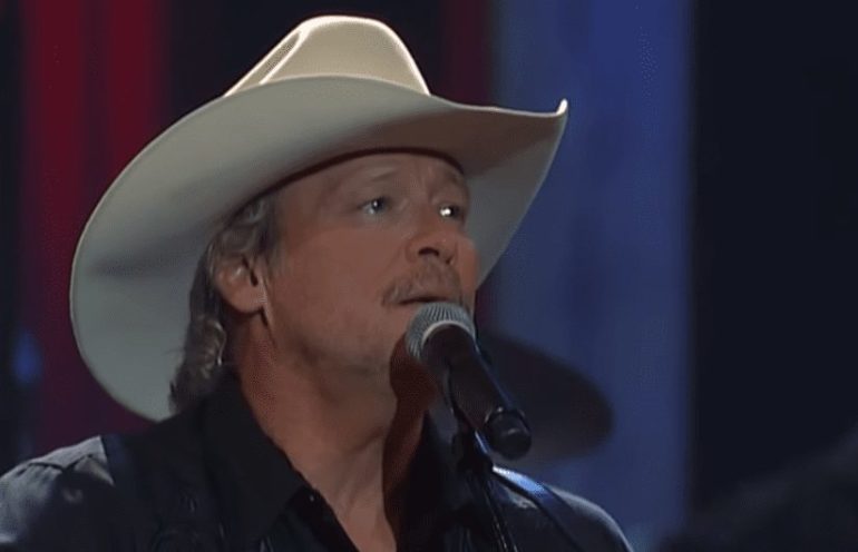 Alan Jackson wearing a cowboy hat and singing into a microphone