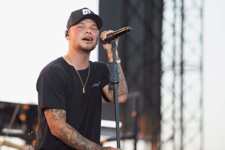 Kane Brown with tattoos holding a microphone
