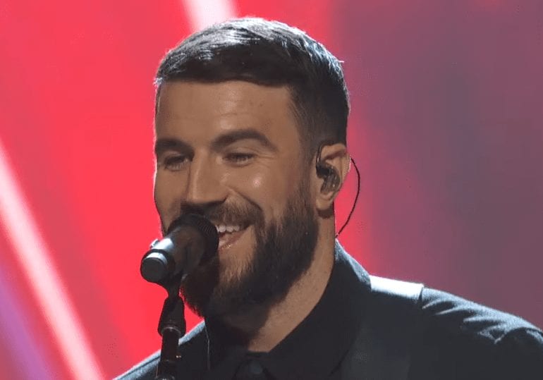 Sam Hunt with a beard and a mustache talking into a microphone