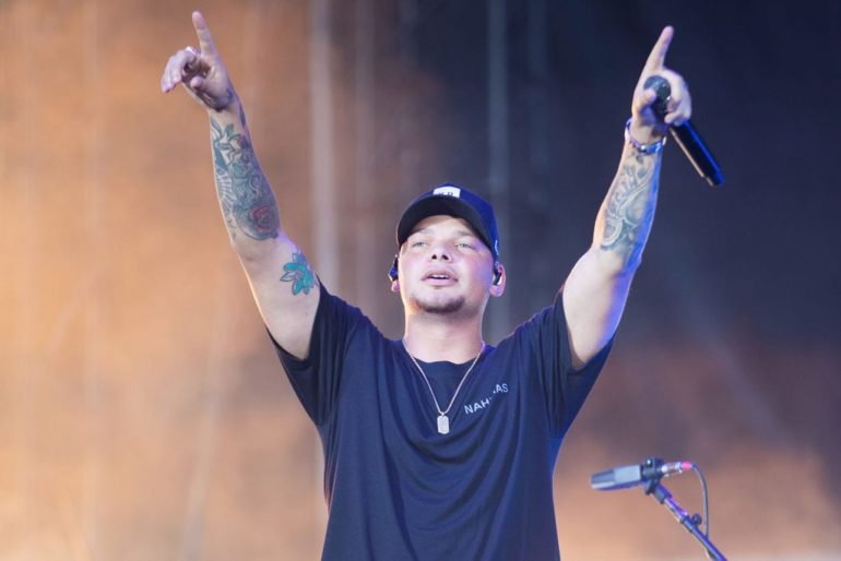 Kane Brown with tattoos on his arm holding a microphone