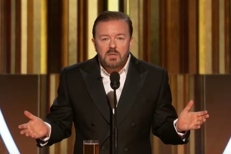 Ricky Gervais in a suit speaking into a microphone