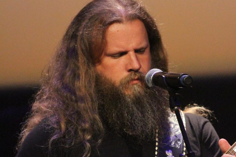 Jamey Johnson with long hair and a beard speaking into a microphone