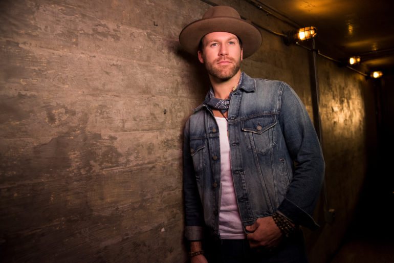 Drake White wearing a hat and standing in front of a wall