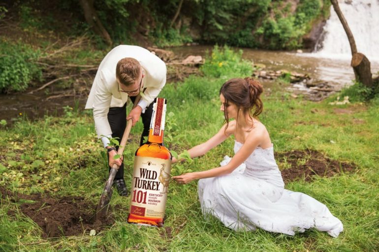 A man and woman in wedding attire holding a bottle of alcohol