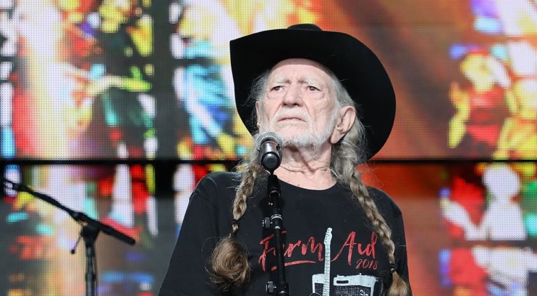 Willie Nelson wearing a hat and a black jacket with a microphone in front of him