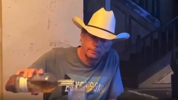 A man wearing a cowboy hat and holding a glass of beer