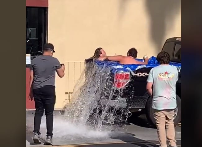 A group of people standing around a car with water splashing on it