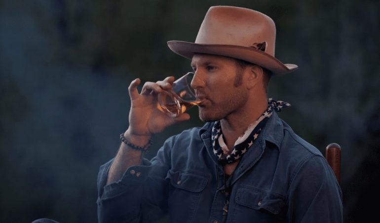 A man in a cowboy hat drinking from a glass