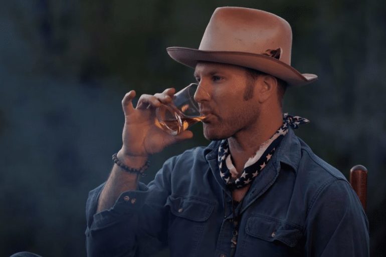 A man in a cowboy hat drinking from a glass