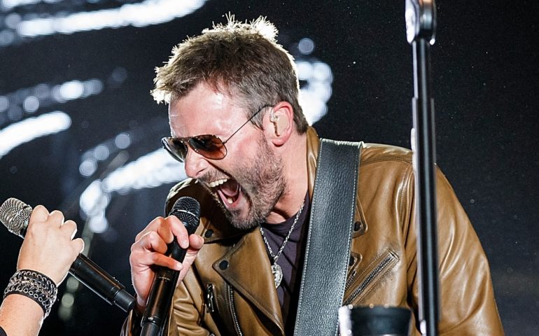 A man with a beard and sunglasses singing into a microphone
