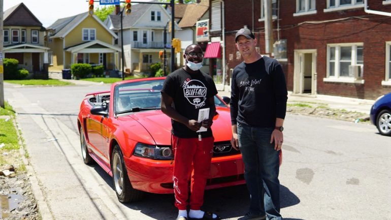 Two men standing next to a red car