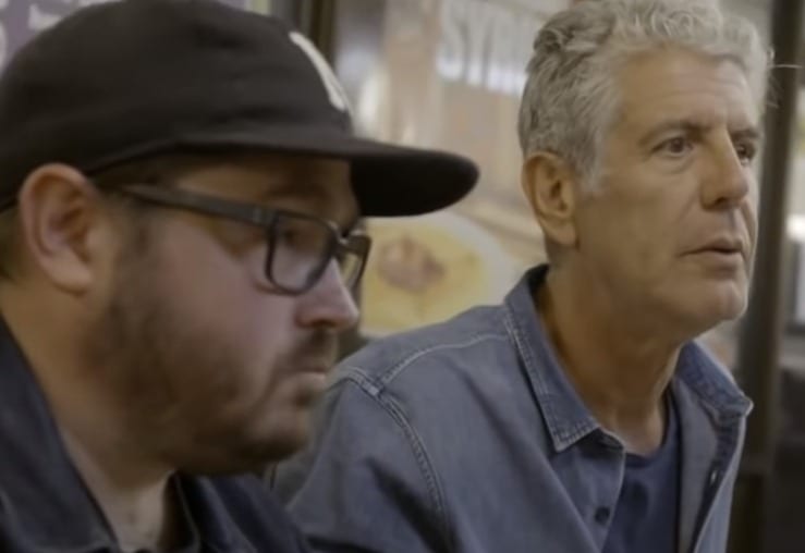Anthony Bourdain in a hat looking at another man