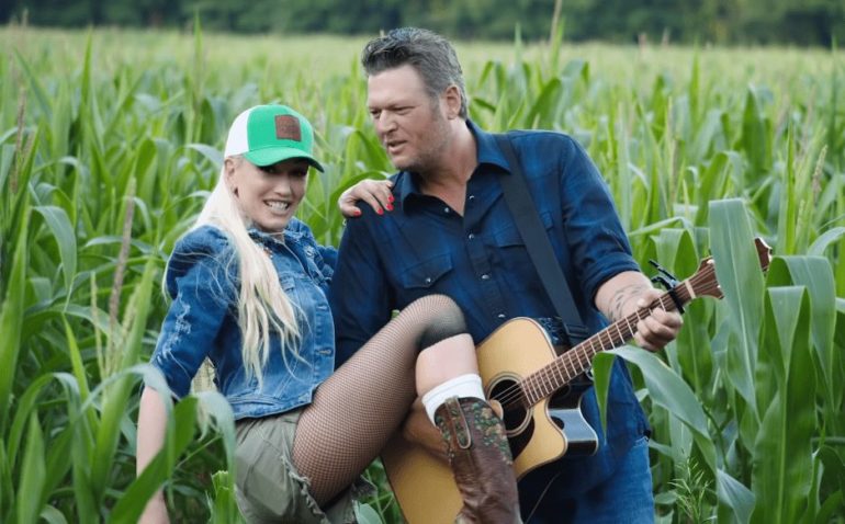 Blake Shelton and woman sitting in a field with a guitar