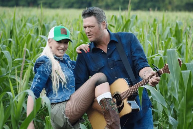 Blake Shelton and woman sitting in a field with a guitar