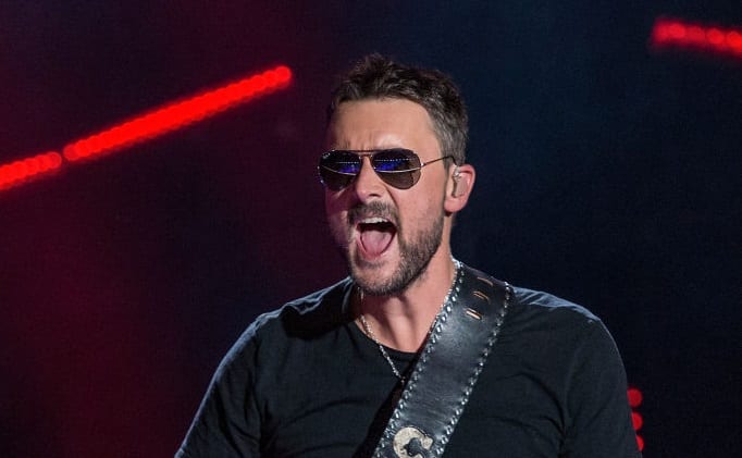 Eric Church with a beard and wearing sunglasses with a microphone in the background