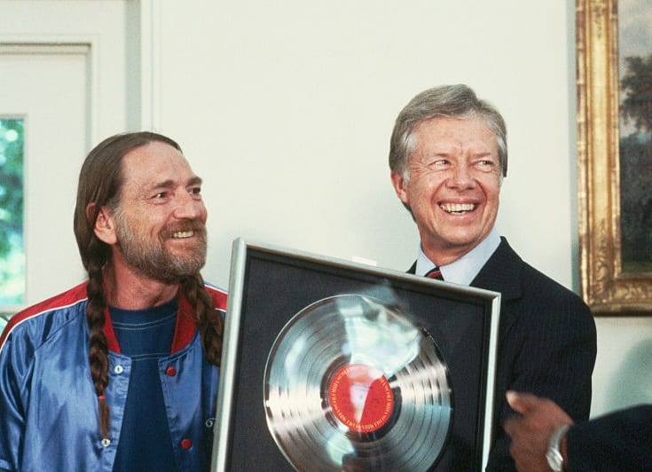 Jimmy Carter smiling next to a person holding a record