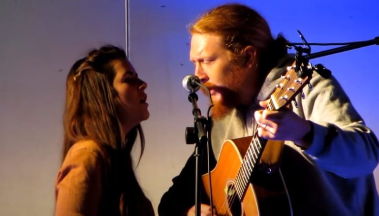 A man playing a guitar next to a woman singing into a microphone