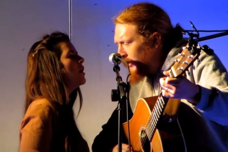 A man playing a guitar next to a woman singing into a microphone
