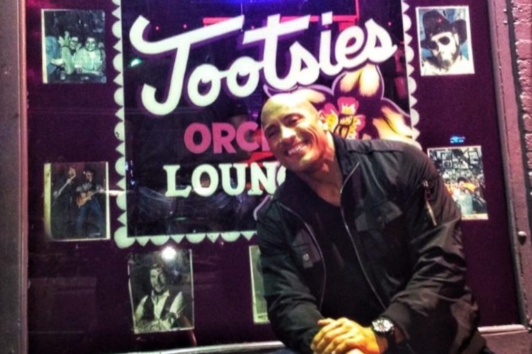 Dwayne Johnson sitting in front of a sign