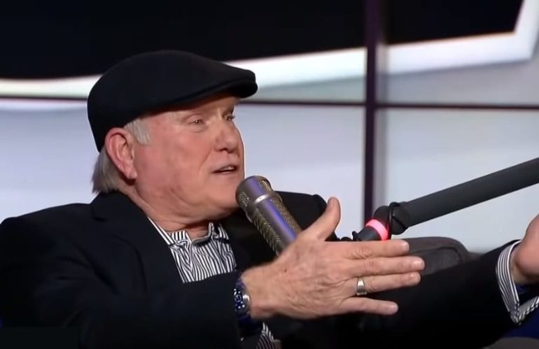 Terry Bradshaw wearing a hat and holding a microphone