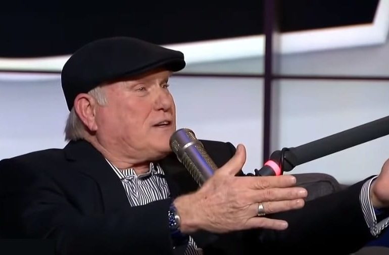 Terry Bradshaw wearing a hat and holding a microphone