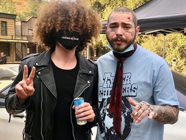 Post Malone with a mask on his face next to a man with a beard