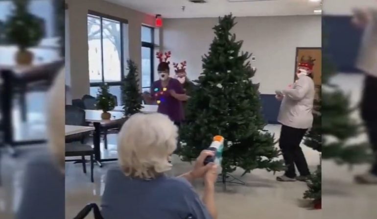 A person holding a camera next to a christmas tree